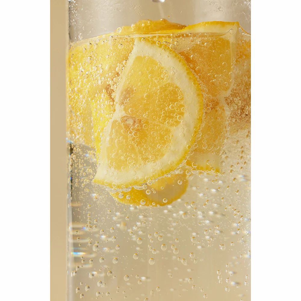 Glas mit gelber Flüssigkeit und Zitronenscheiben. Blasen im Glas.