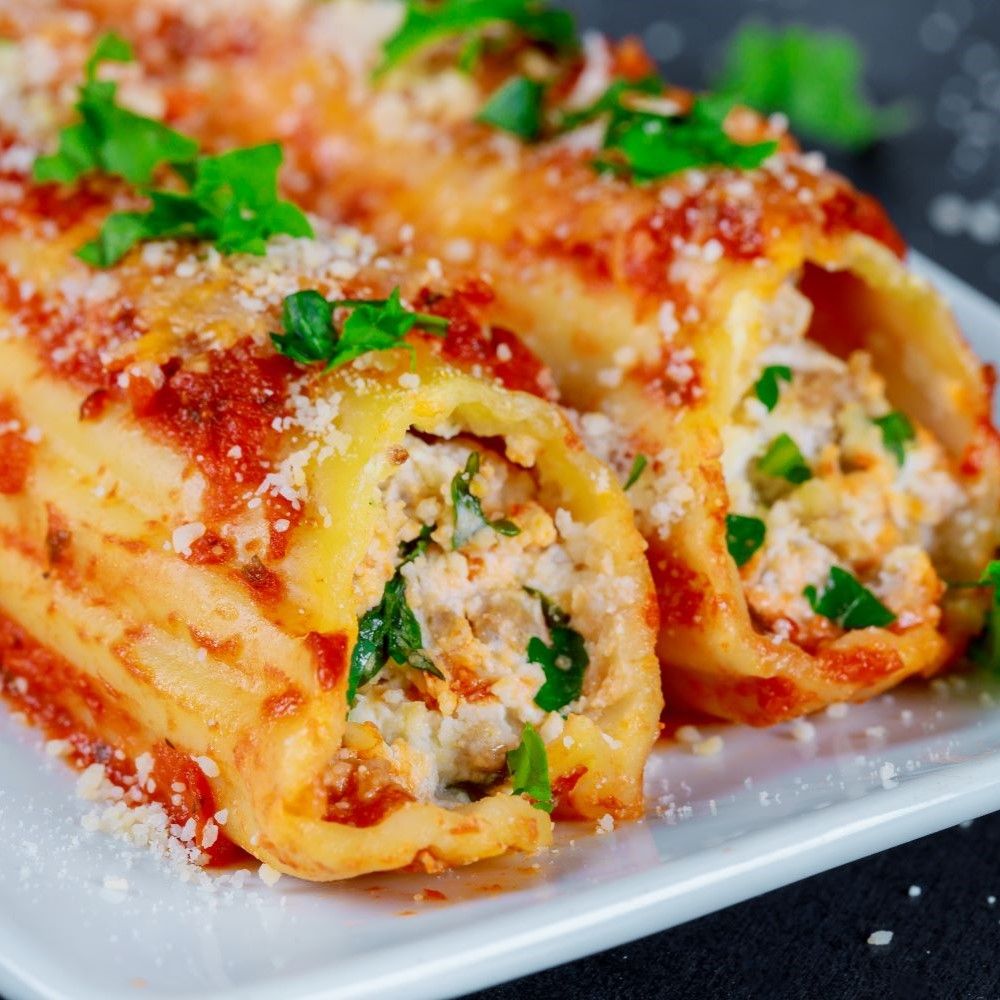 Cannelloni mit Tomatensauce und Käse auf einem Teller. Gehackte Kräuter als Garnitur.