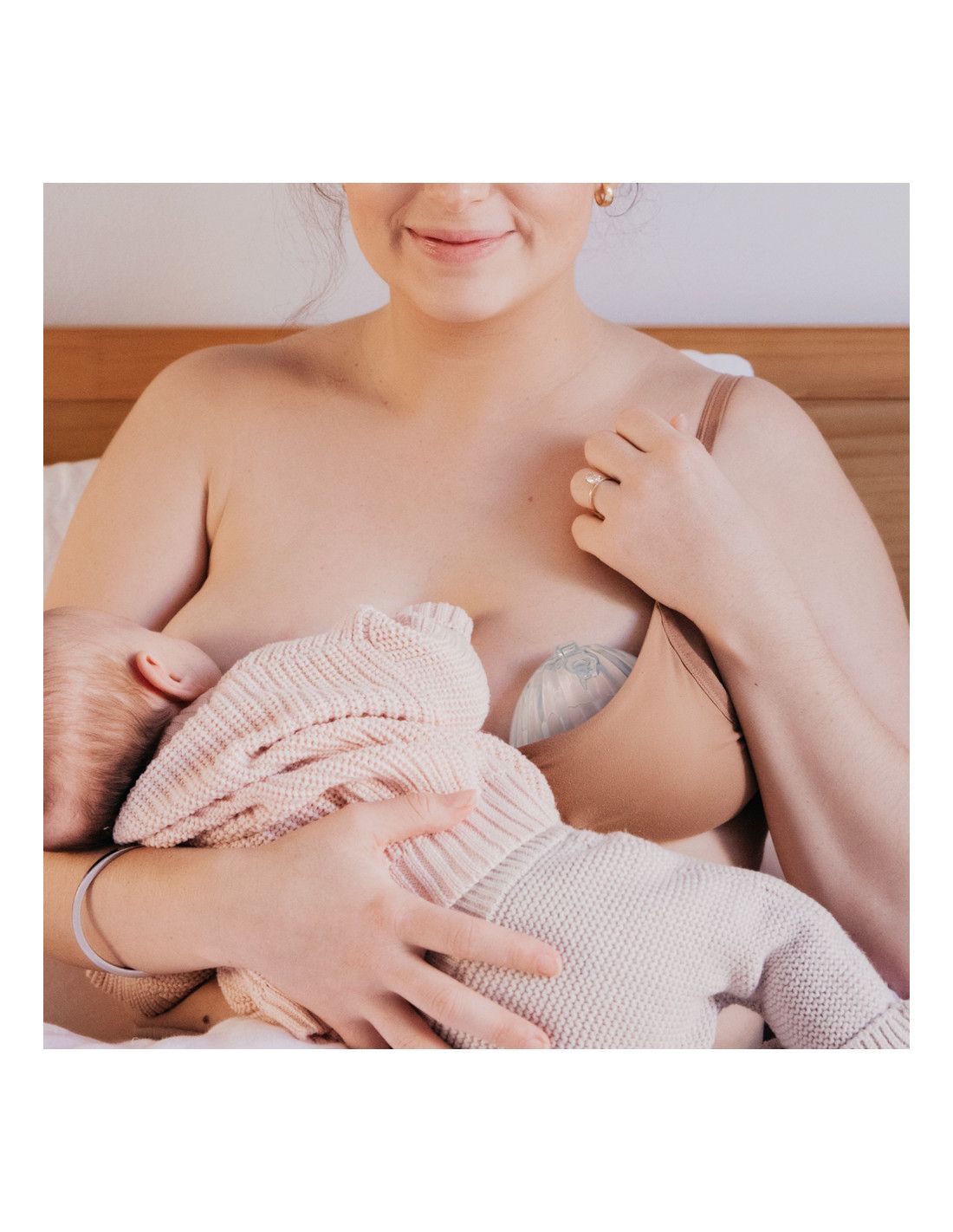Eine Frau stillt ein Baby, während sie eine transparente, muschelförmige Milchpumpe in ihrem BH trägt.