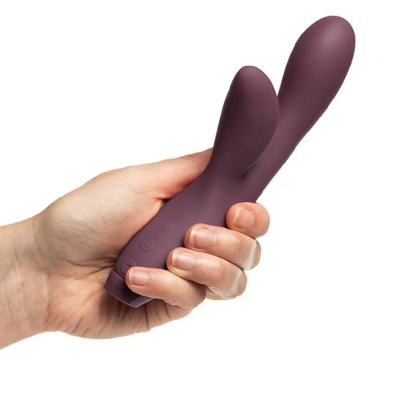 Hand hält lila Vibrator in Hasenform. Zwei Ohren, gebogene Form. Weißer Hintergrund.