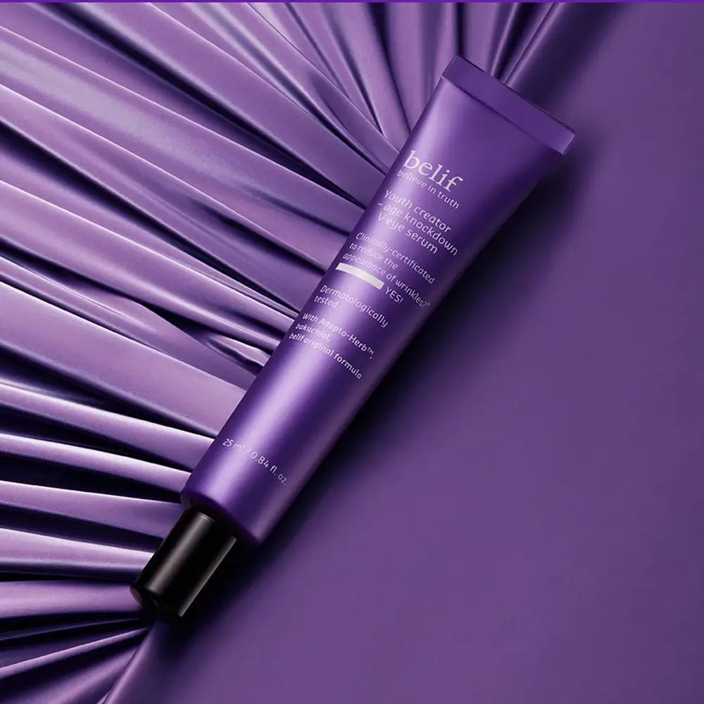 Lila Tube mit schwarzem Deckel. Aufschrift: belif, Youth creator - age knockdown V eye serum. Auf lila Hintergrund.