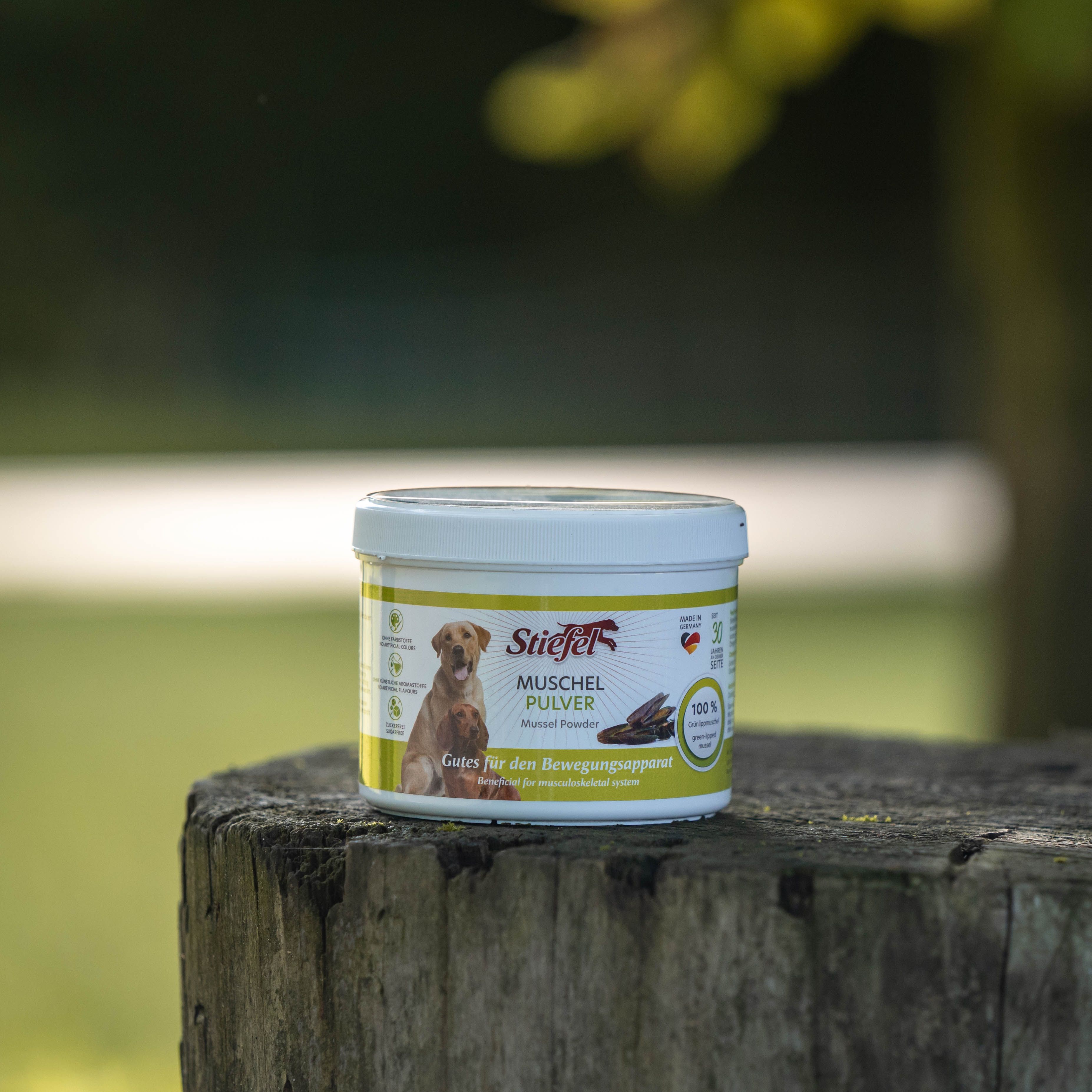 Weißer Behälter mit Stiefel Muschelpulver auf einem Baumstumpf. Das Produktetikett zeigt Logo und Produktinformationen.