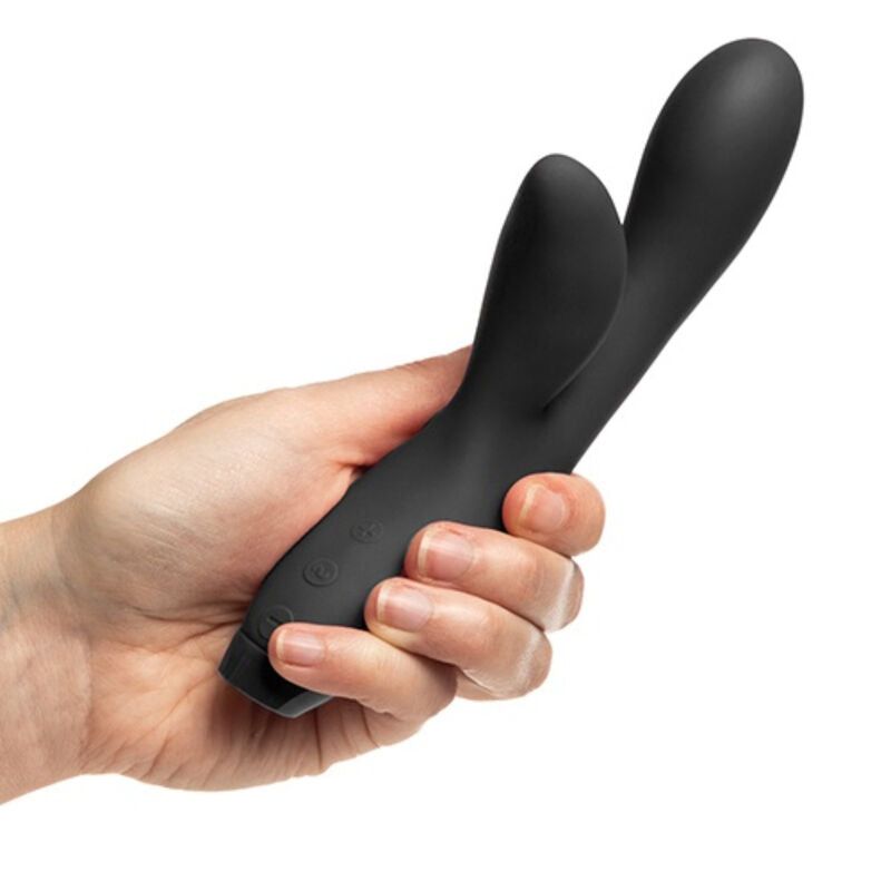 Schwarzer Vibrator in einer Hand gehalten. Form: gebogen mit zwei Enden. Material: Silikon. Knöpfe sichtbar.