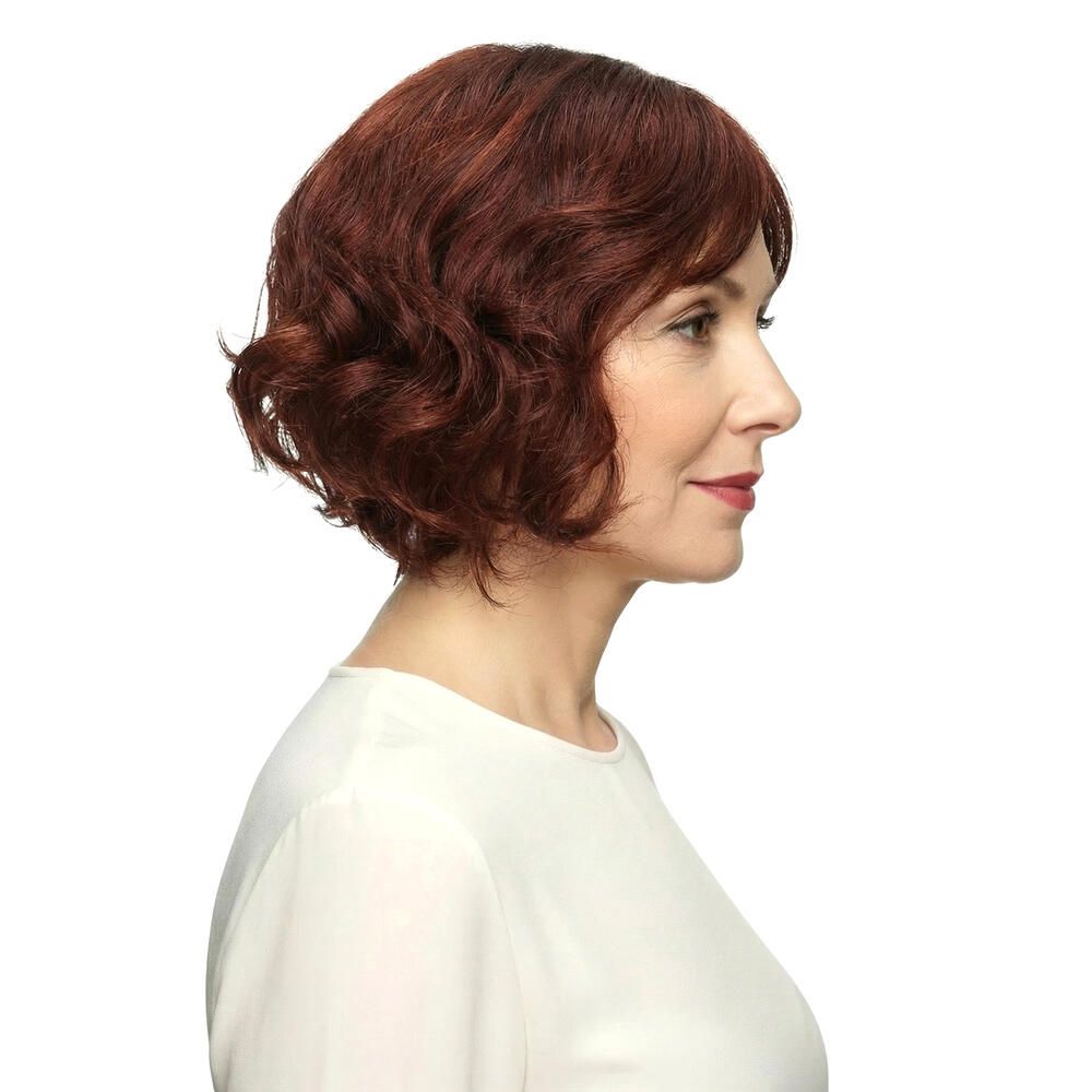 Frau mit rotbrauner, gewellter Perücke. Blick zur Seite, vor weißem Hintergrund.