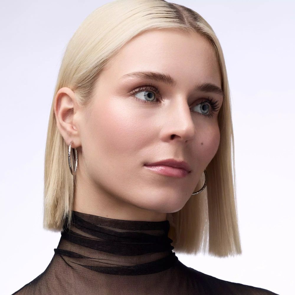 Porträt einer Frau mit blonden Haaren. Sie trägt silberne Creolen. Aufgetragenes Make-up.