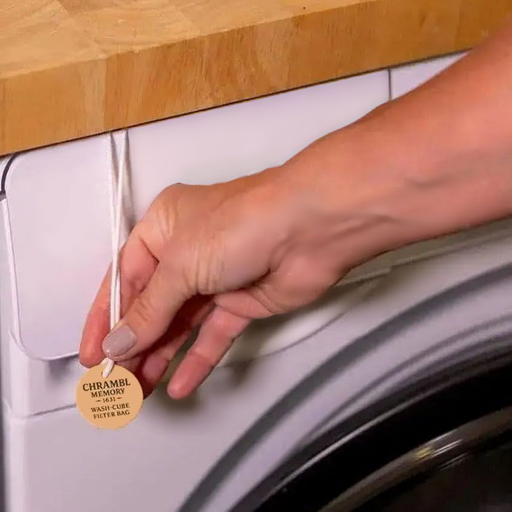 Hand hält einen runden, holzähnlichen Anhänger mit Produktinformationen. Aufschrift: CHRAMBL, Waschmittel-Filterbeutel.