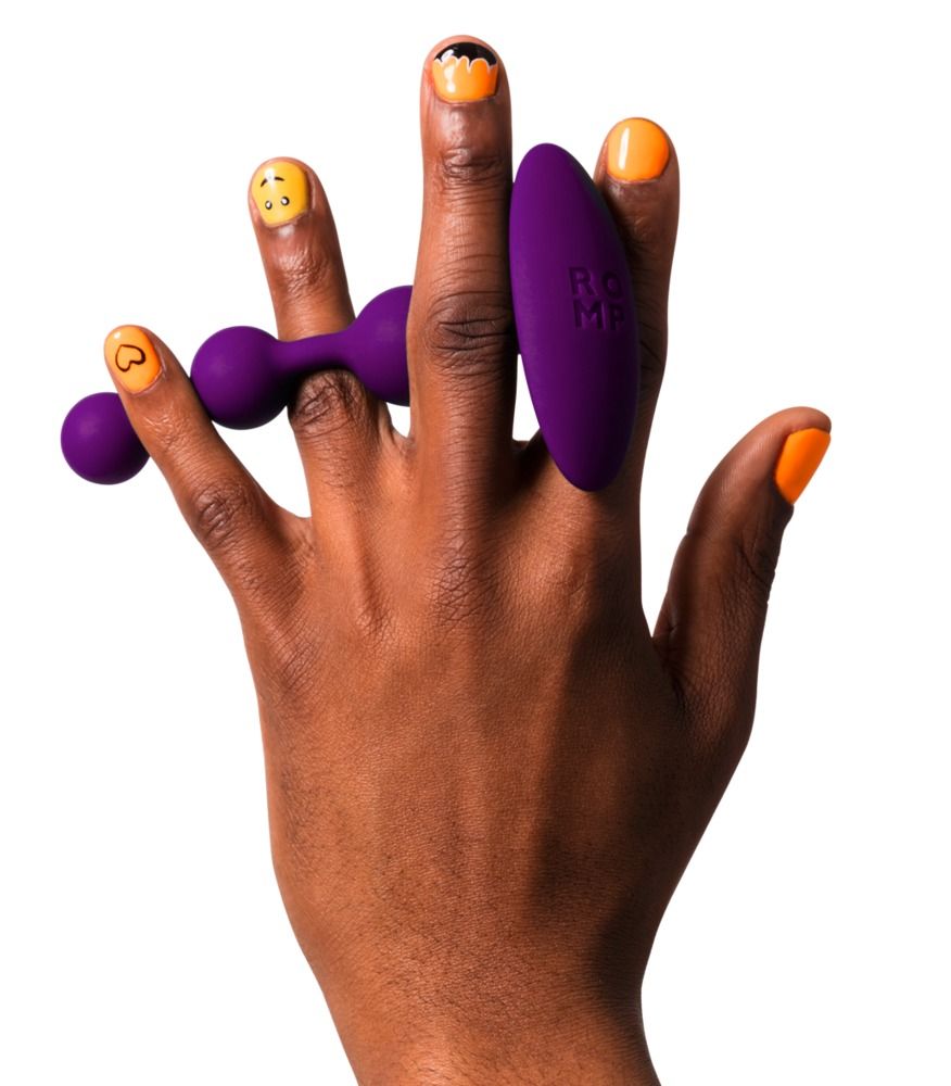 Lila Analperlen und ein Vibrator in einer Hand. Gelbe und orangefarbene Nagelkunst.