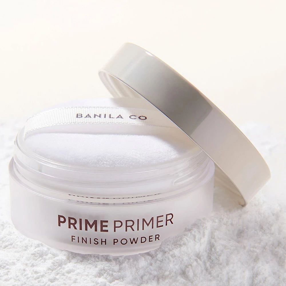 Weißer Tiegel mit Deckel und Puderquaste. Aufschrift: PRIME PRIMER FINISH POWDER. Puder auf weißem Untergrund.