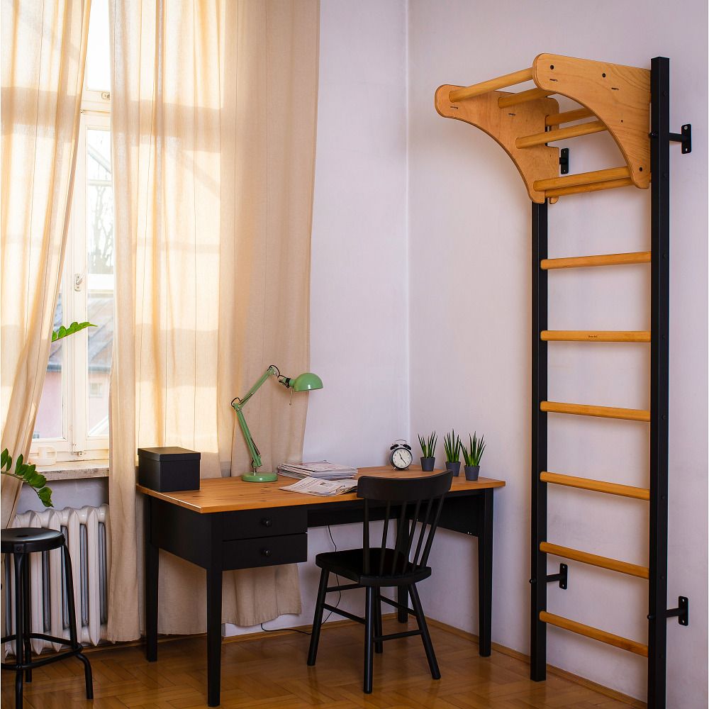 Sprossenwand mit Klimmzugbügel, Holz und Metall. An Wand montiert, neben Schreibtisch. Fenster im Hintergrund.