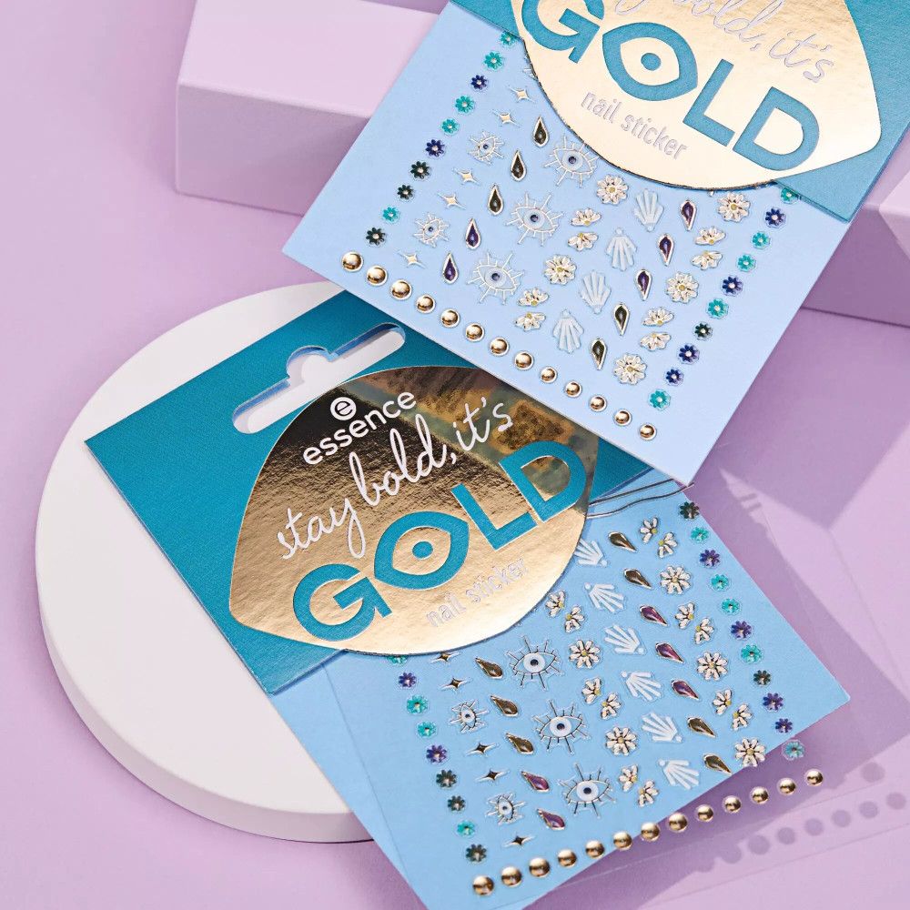 Zwei Packungen Nagelsticker mit goldenen und farbigen Designs. Marke: Essence. Auf blauem Hintergrund.
