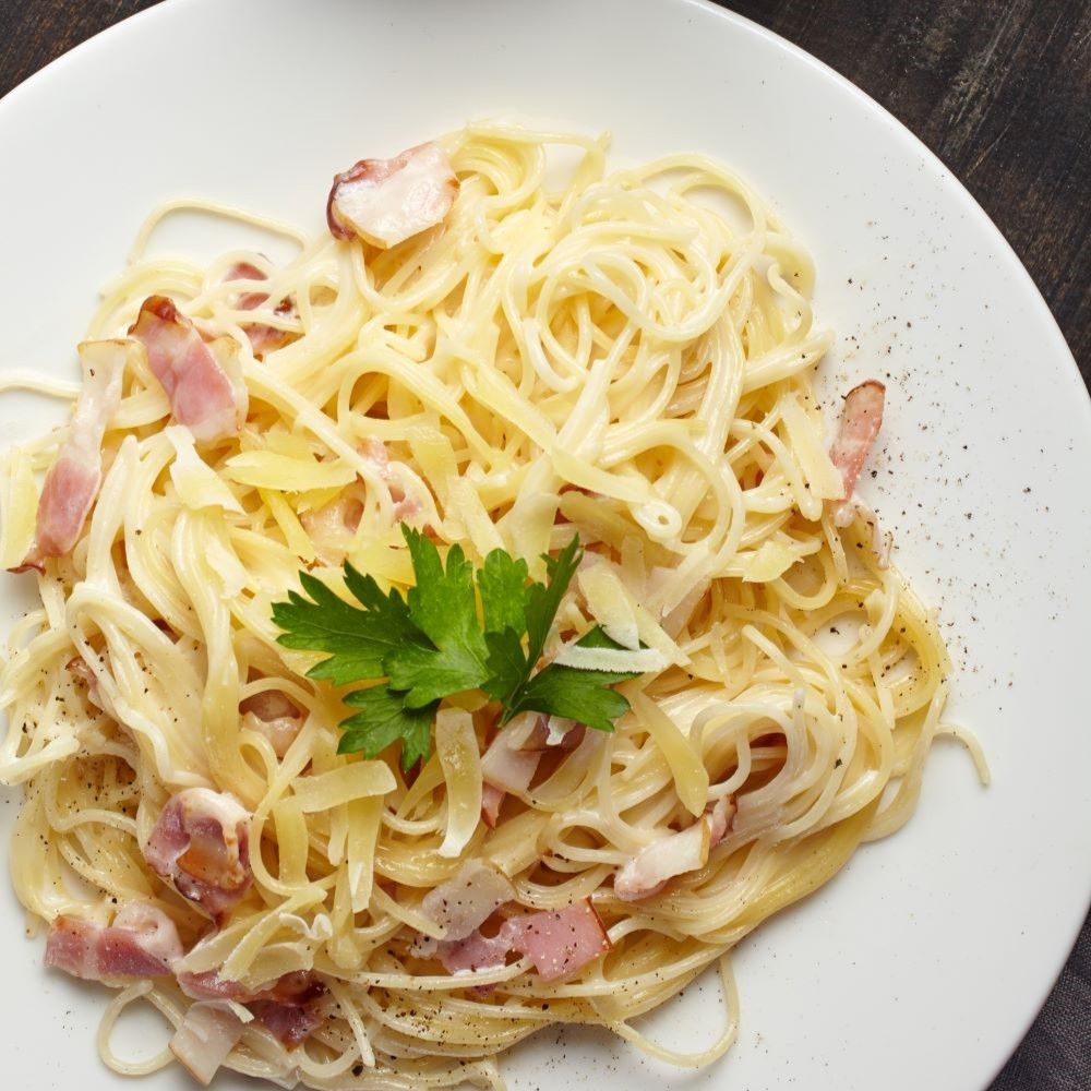 Spaghetti Carbonara auf weißem Teller. Mit Speck, Käse und Petersilie garniert. Draufsicht.