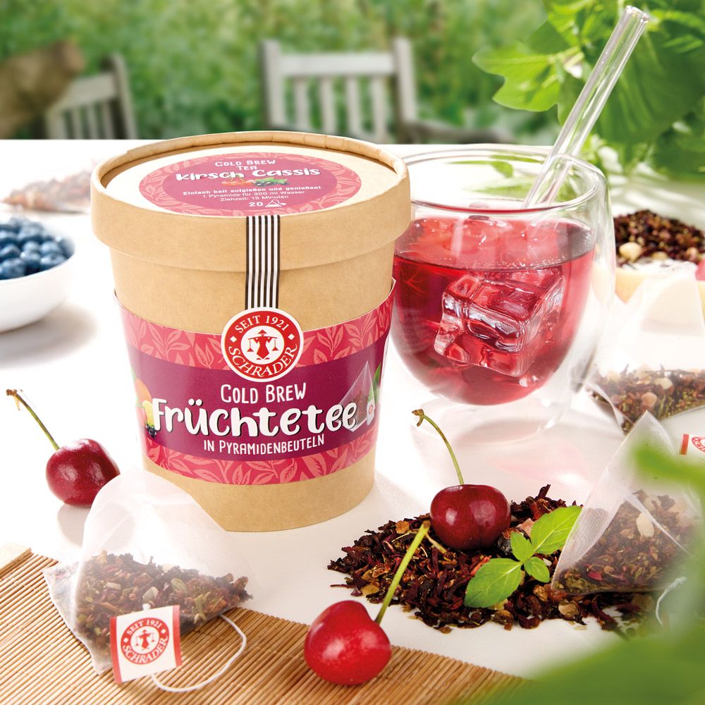 Produktverpackung mit Kirschen, Teebeuteln und Glas mit Getränk. Aufdruck: Cold Brew Früchtetee Kirsch-Cassis. Logo und Schriftzug Schrader.