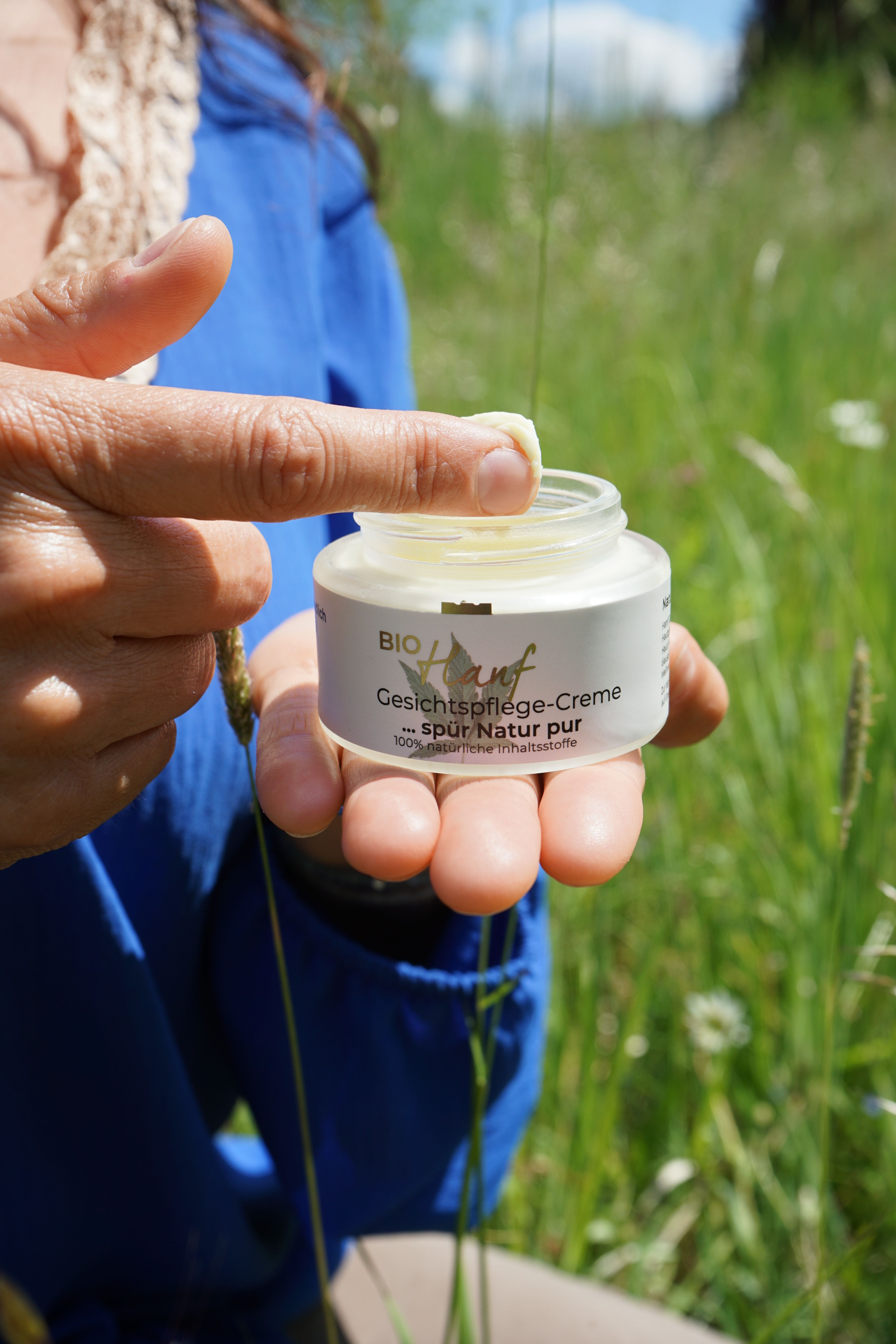 Eine Hand entnimmt einer Creme-Dose mit Bambusdeckel eine kleine Menge Creme mit dem Finger.