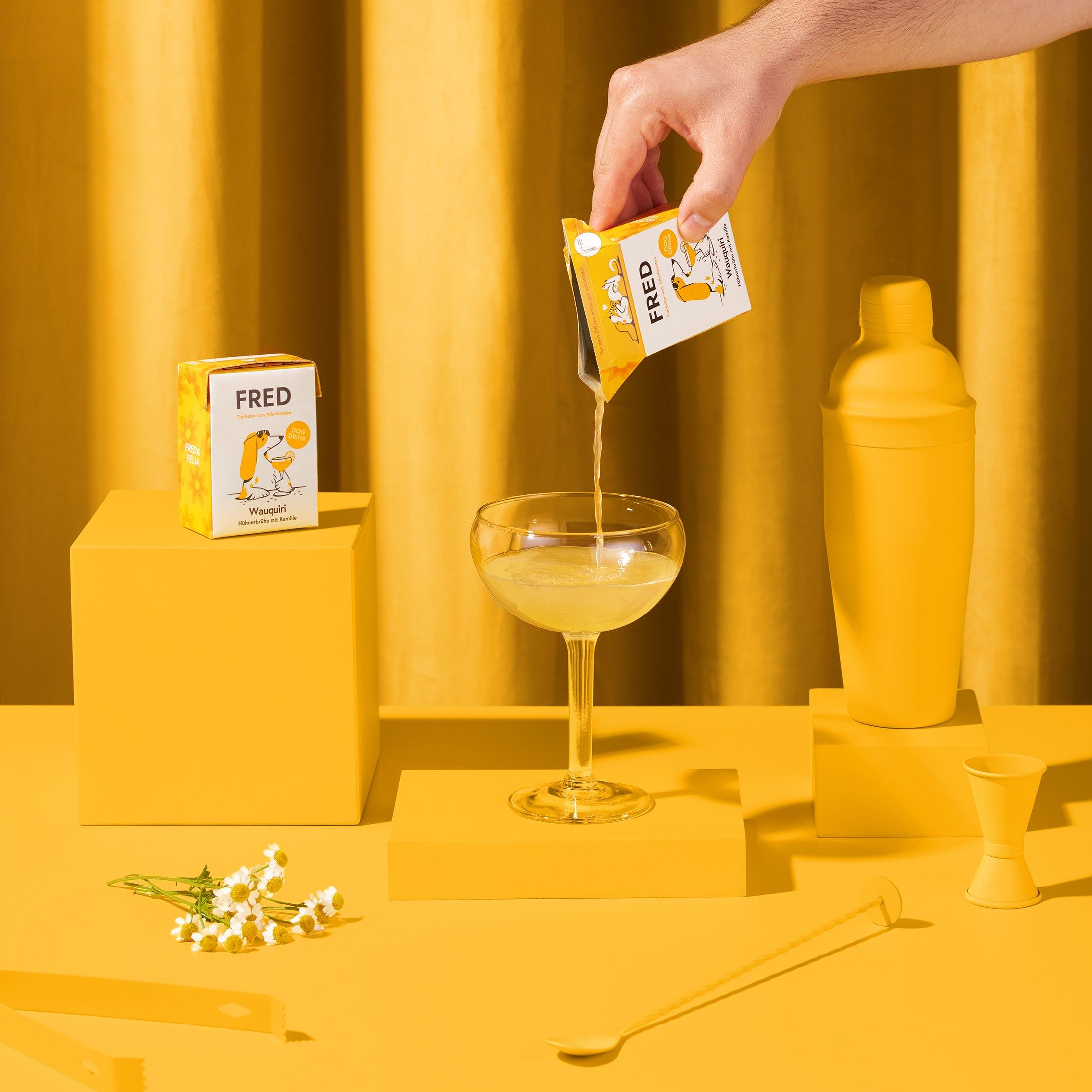 FRED Dog Drink wird in ein Glas gegossen. Gelbes Set mit Cocktail-Utensilien. Hintergrund: gelber Stoff.