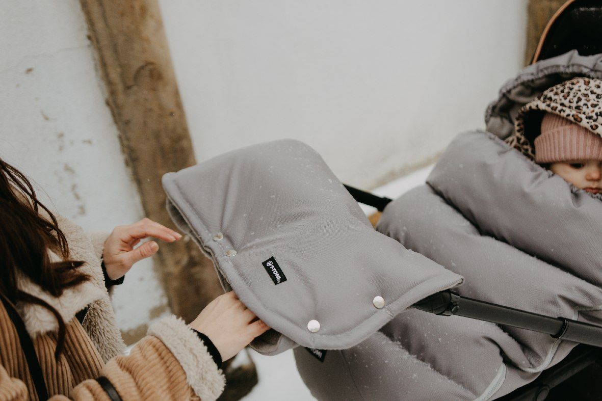Graue, gepolsterte Kinderwagen-Handwärmer mit weißen Tupfen und Druckknöpfen. Ein kleines schwarzes Etikett mit einer weißen '1'.