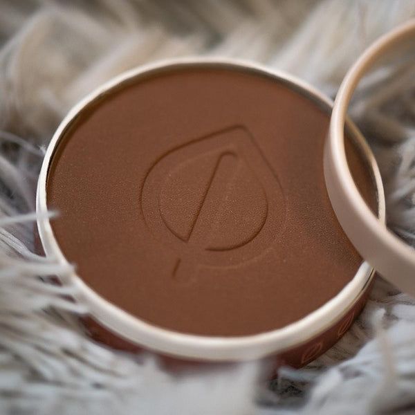 Runder Behälter mit braunem Bronzing Powder. Geprägtes Logo. Goldfarbener Rand. Auf flauschigem Untergrund.