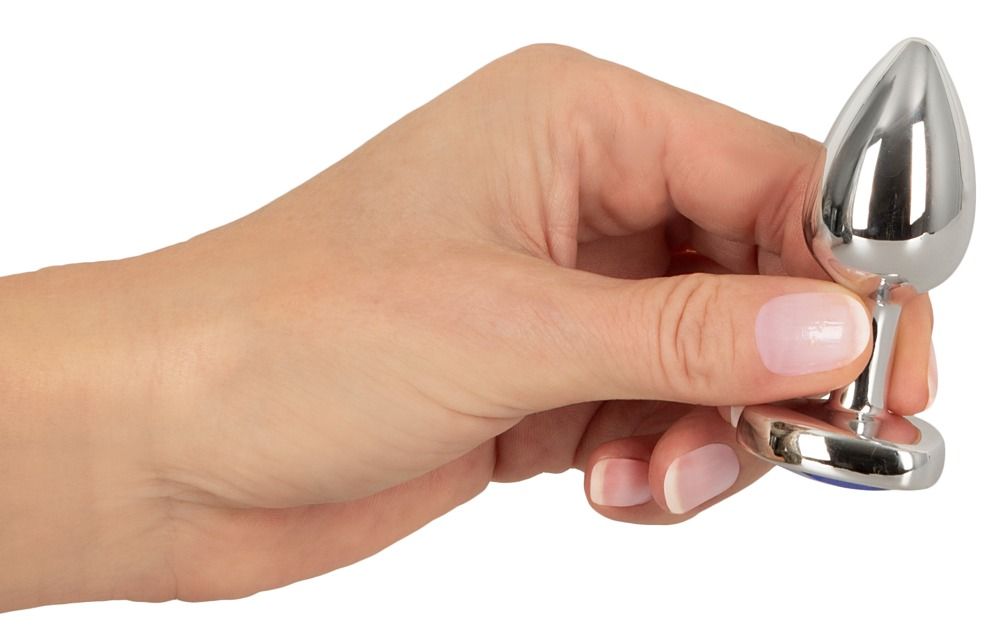 Hand hält silberfarbenen Analplug. Tropfenförmiger Kopf, herzförmige Basis. Glänzende Oberfläche.