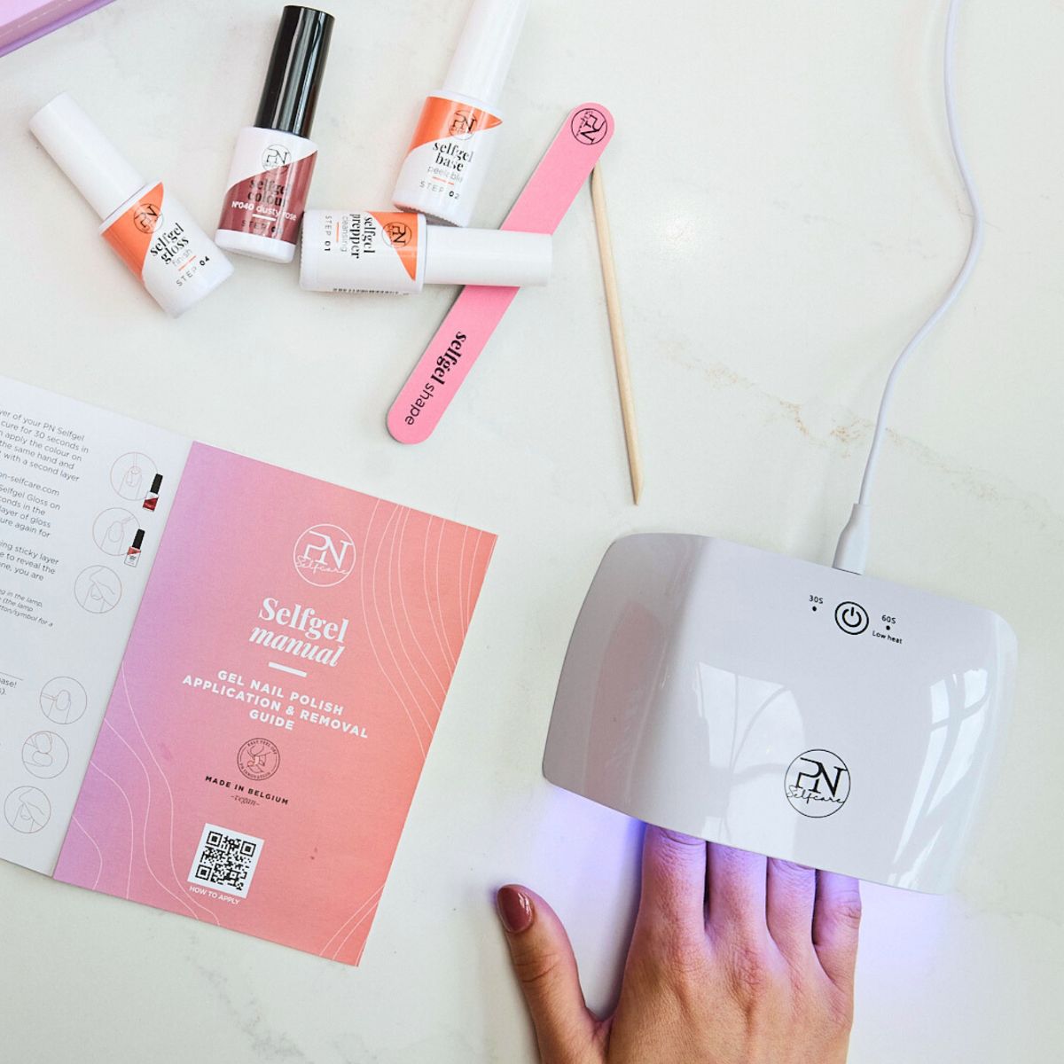 Maniküre-Set mit UV-Lampe, Broschüre, Feile und Flaschen. Aufschrift: selfgel manual. PN-Logo.