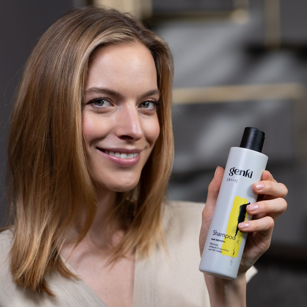 Frau hält Genki Shampoo-Flasche. Weiß, schwarzer Deckel, gelbes Design. Schriftzug: Genki, Shampoo, Hair Growth.