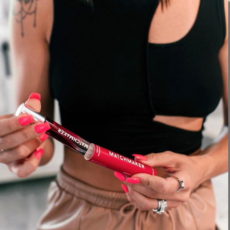Person hält eine rote Parfümflasche mit der Aufschrift "MATCHMAKER" und eine rote Verpackung.
