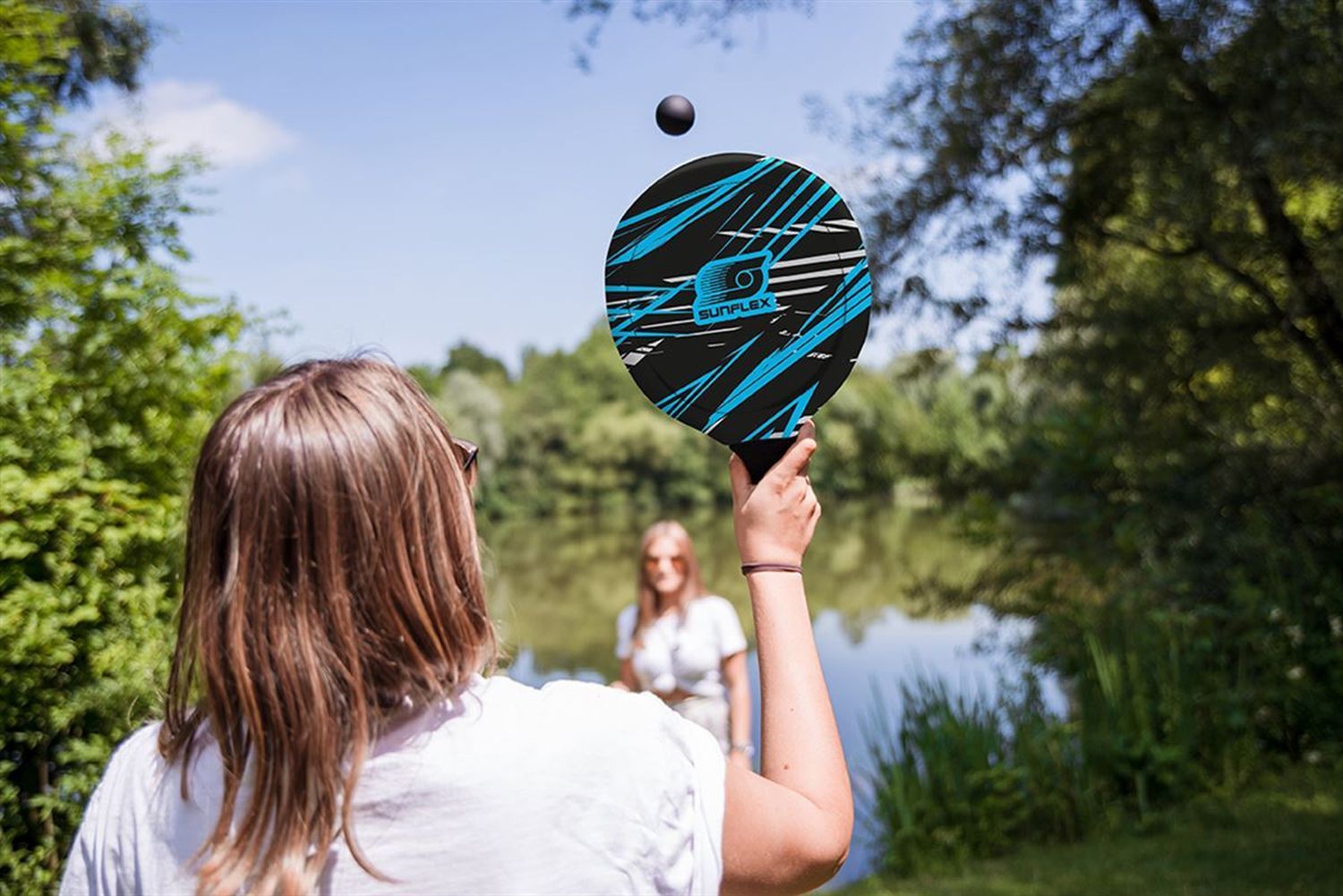 Eine Person hält einen Schläger mit einem Ball in der Luft. Der Schläger hat ein blau-schwarzes Muster und das Logo SUNFLEX.