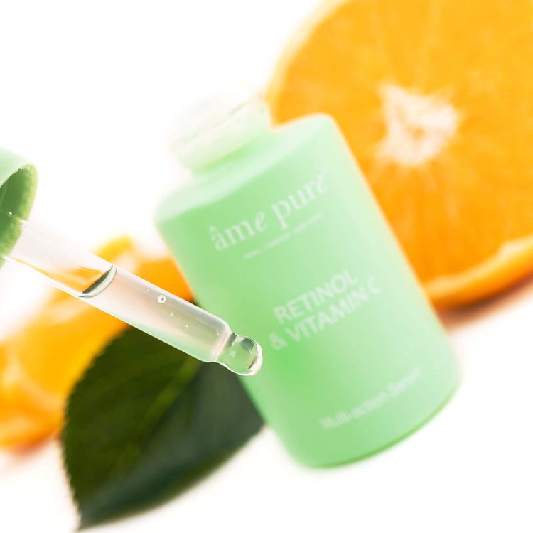 Groene fles met serum en pipet. Op de fles staat 'Retinol & Vitamin C' en 'âme pure'. Er ligt een sinaasappelschijfje naast.
