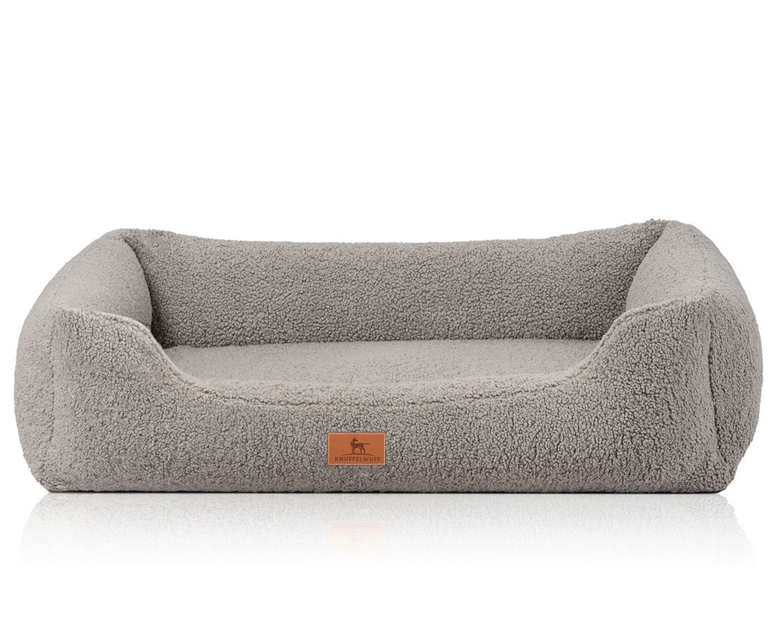 Orthopädisches Hundebett in Grau. Rechteckige Form mit erhöhten Seiten. Weiches, flauschiges Material. Kleines Markenlogo.