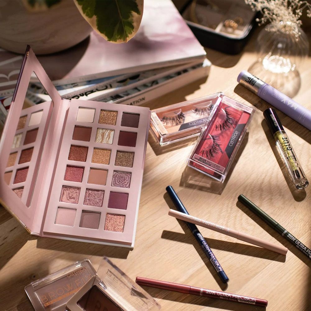 Make-up-Produkte auf Holzoberfläche. Enthalten: Lidschattenpalette, Wimpern, Eyeliner, Mascara. Marke: Catrice.