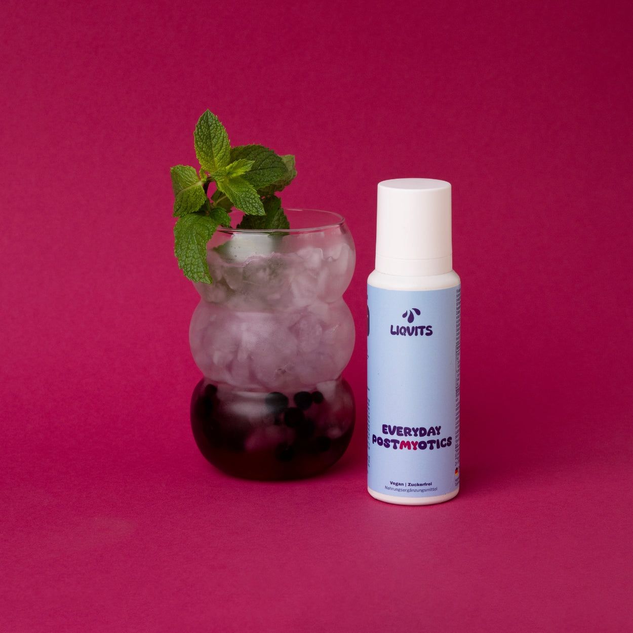 Glas mit Eiswürfeln und Minze. Daneben blaue Flasche mit weißem Deckel. Aufschrift: LIQVITS, Everyday POSTMYOTICS.