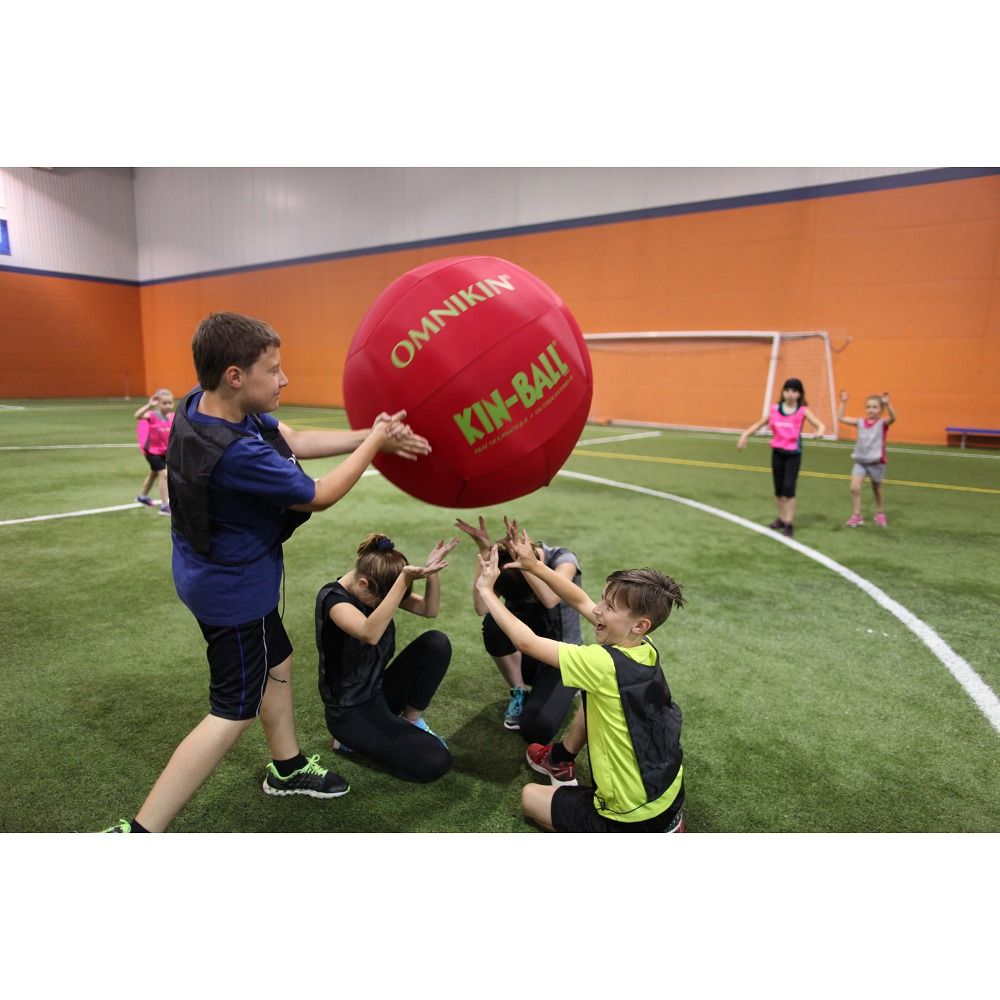 Roter Kin-Ball. Mehrere Kinder spielen in einer Sporthalle. Das Produkt wird von mehreren Kindern gehalten.