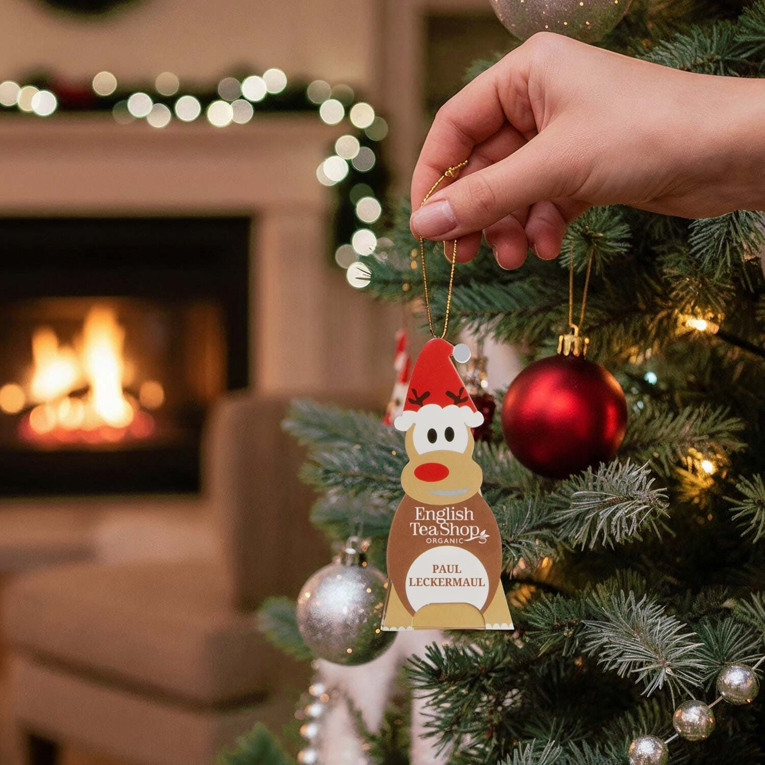 Hand hält einen weihnachtlichen Tee-Anhänger in Form eines Rentiers am Weihnachtsbaum.