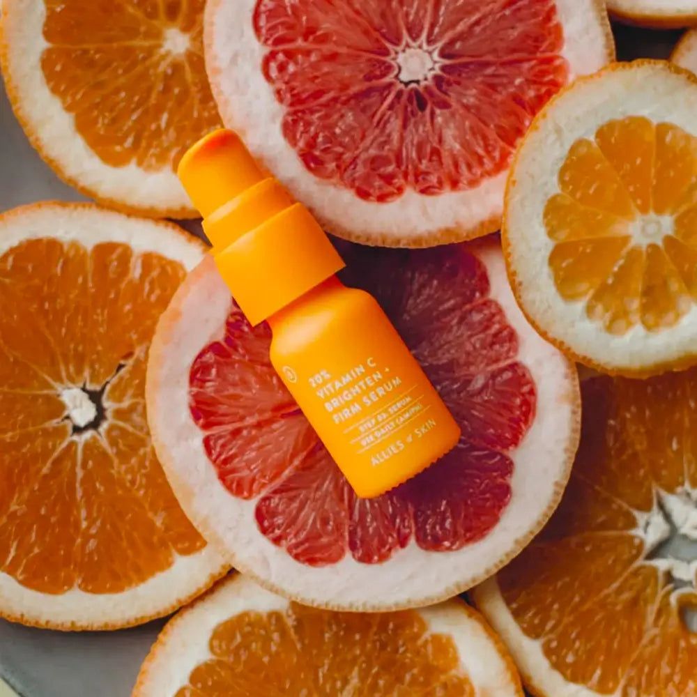 Orangefarbenes Serumfläschchen auf Grapefruit- und Orangenscheiben. Aufschrift: 20% Vitamin C Brighten + Firm Serum. Marke: Allies of Skin.