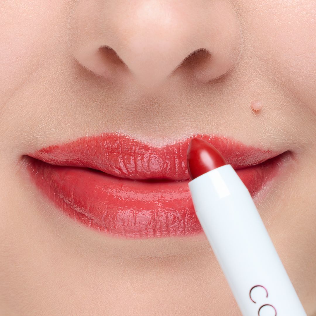 Lippenstift wird auf Lippen aufgetragen. Roter Lippenstift in weißer Hülle. Lippen sind mit rotem Lippenstift bemalt.