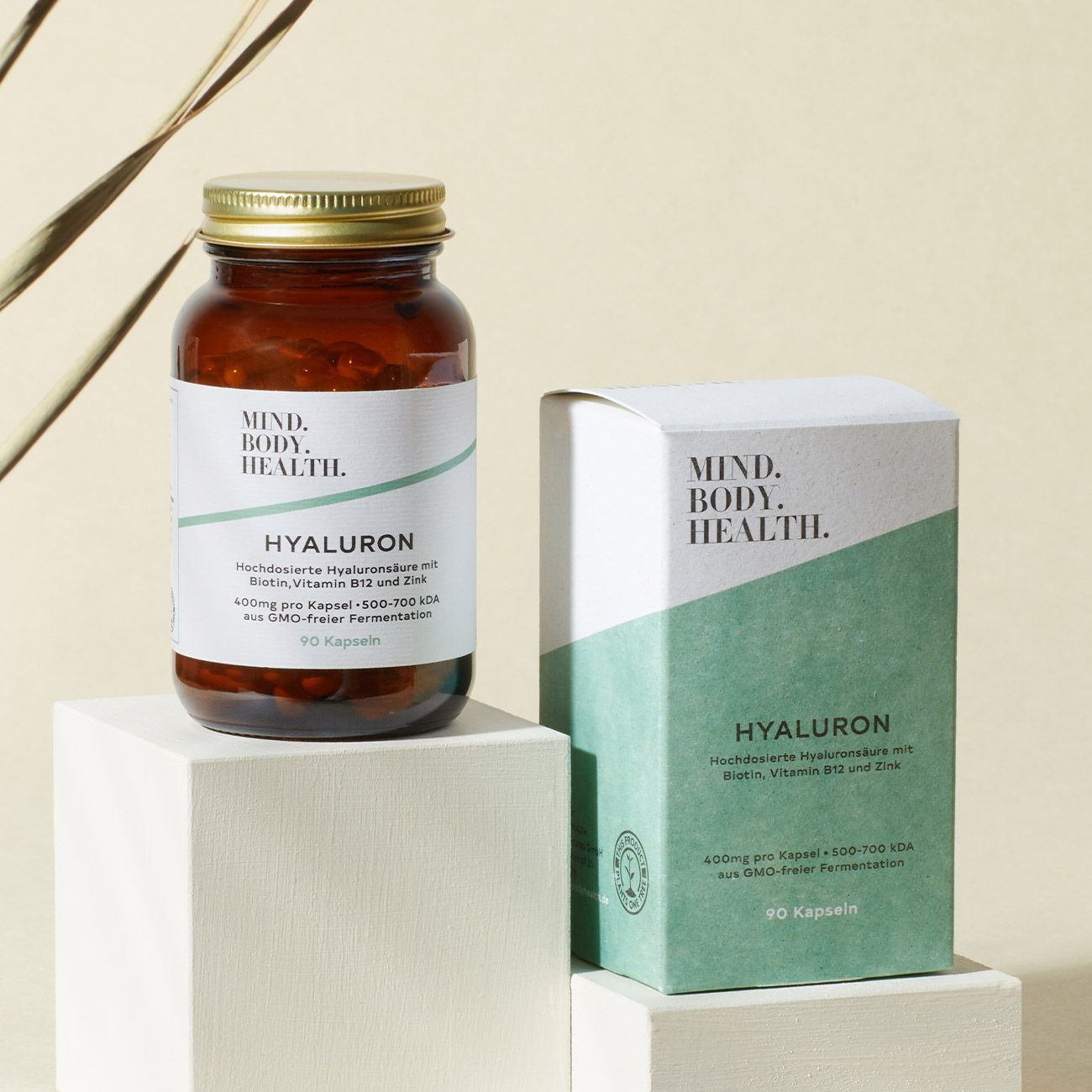 Braune Glasflasche und Schachtel mit Produktnamen. Beide auf weißem Podest. Etiketten mit Inhaltsangaben.