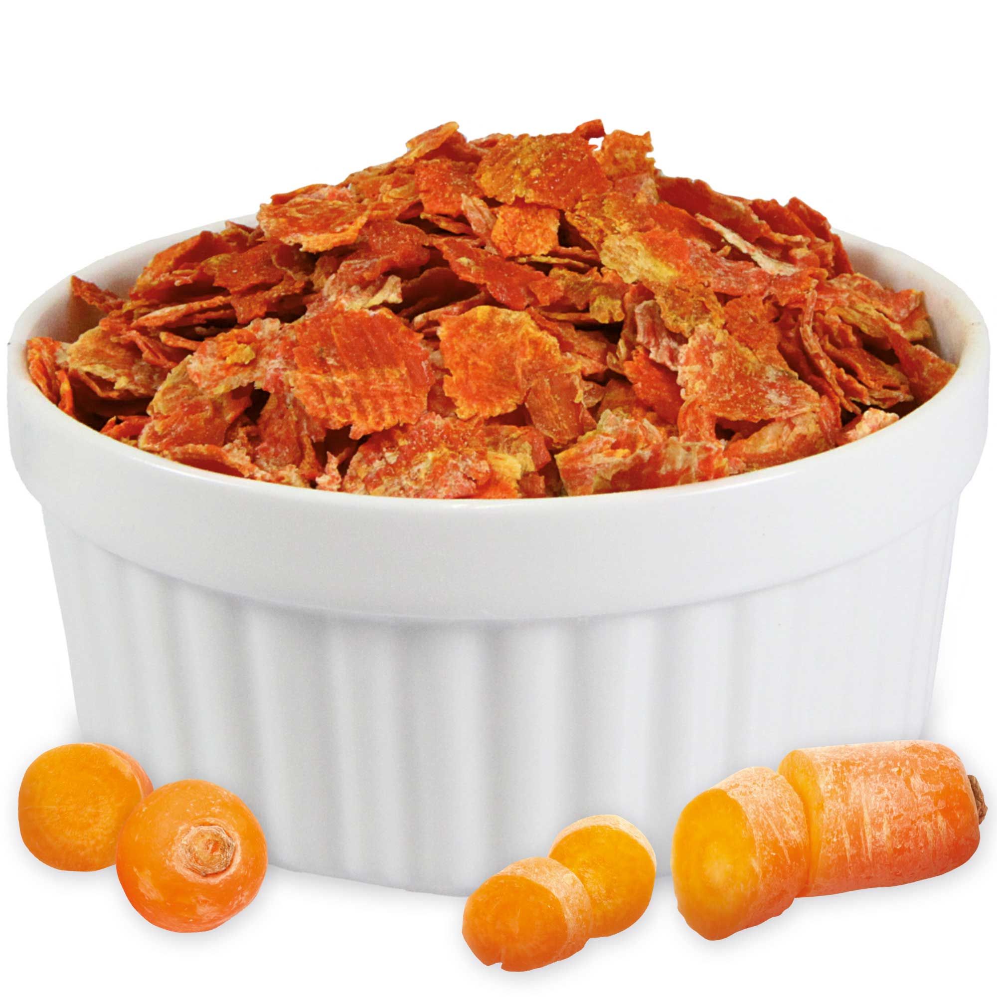 Weiße Schale mit geriffelter Außenseite, gefüllt mit orangefarbenen Karottenflocken. Daneben Karottenstücke.
