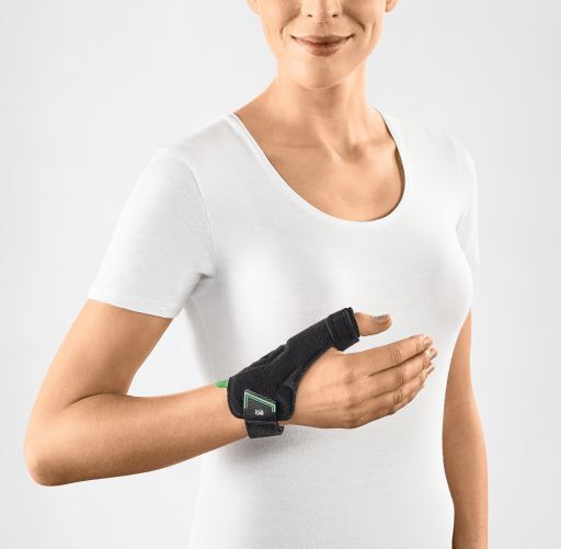 Person trägt eine schwarze Daumenorthese. Die Orthese bedeckt Daumen und Handgelenk. Grünes Element am Handgelenk.