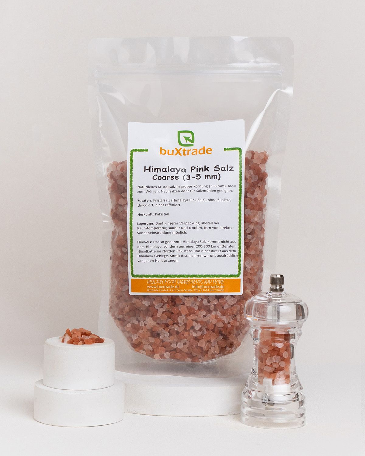 Ein Beutel mit grobem Himalaya-Salz, ein weißer Zylinder mit Salz und eine Salzmühle auf weißem Hintergrund.