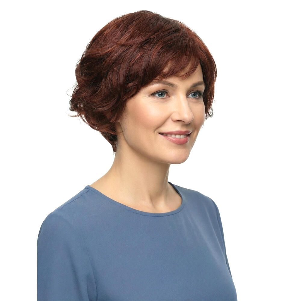 Frau mit roter Perücke. Kurzer, gewellter Haarschnitt. Blauer Pullover. Dreiviertelansicht.