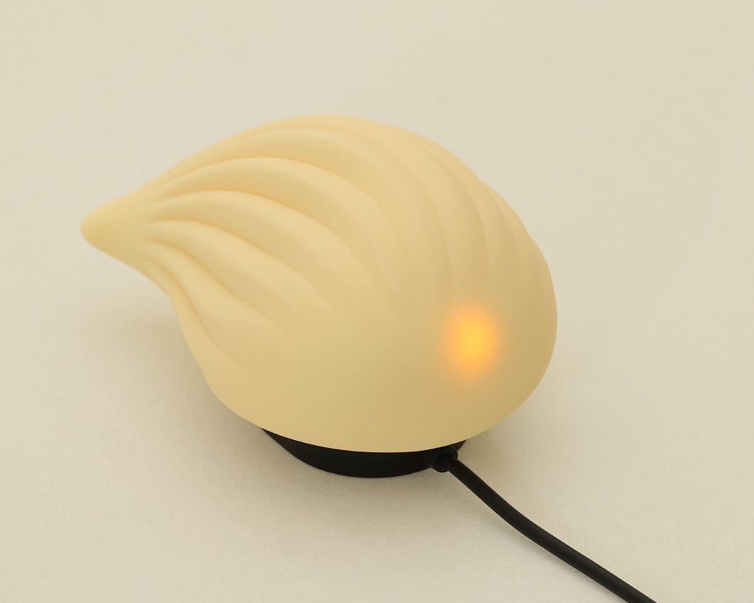 Beigefarbener Vibrator in Tropfenform mit geriffelter Oberfläche. Ein gelbes Licht leuchtet. Schwarzes Kabel.