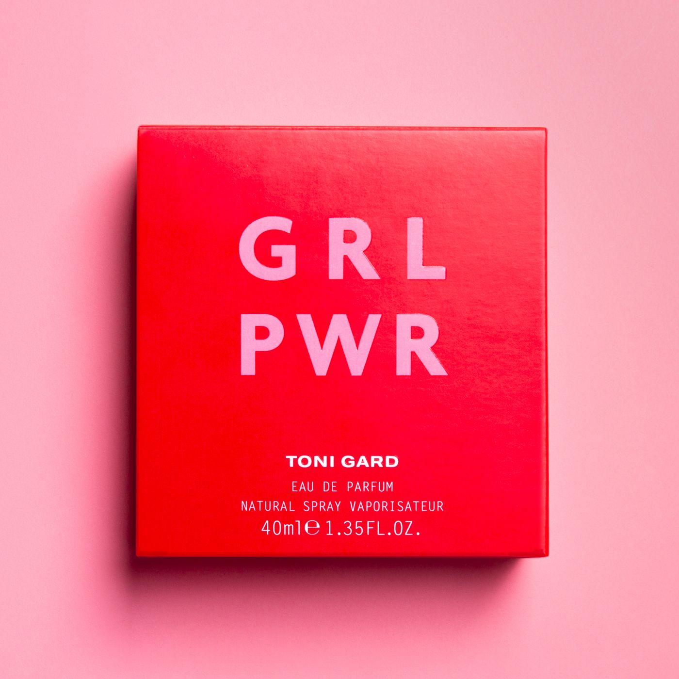 Rote quadratische Verpackung mit weißem Text: GRL PWR. Text: TONI GARD, Eau de Parfum, 40ml 1.35FL.OZ. Rosa Hintergrund.