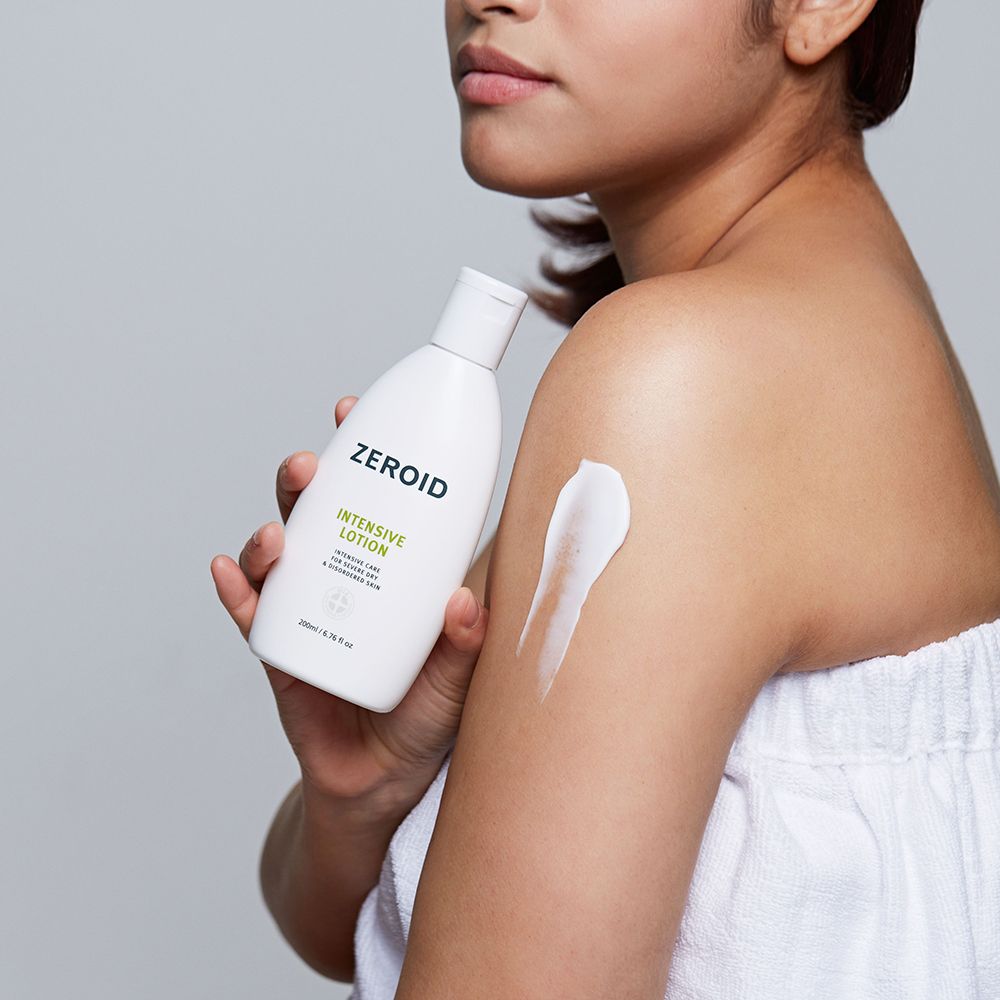 Frau trägt ZEROID Intensive Lotion auf. Weiße Flasche, Text: Intensive Lotion. Creme auf Schulter aufgetragen.