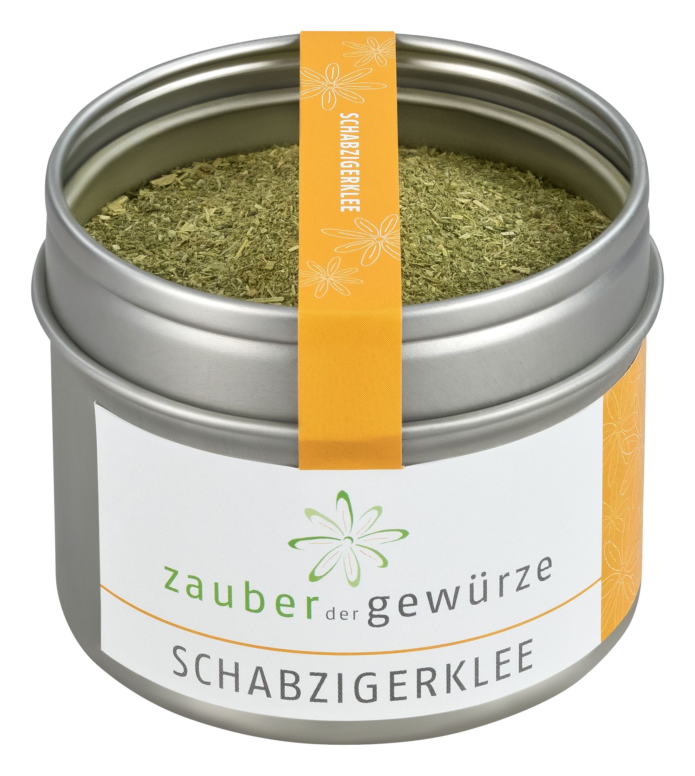 Runde Dose mit Schabzigerklee. Metallbehälter mit weißem Etikett und orangefarbenem Band. Aufschrift: Zauber der Gewürze, Schabzigerklee.