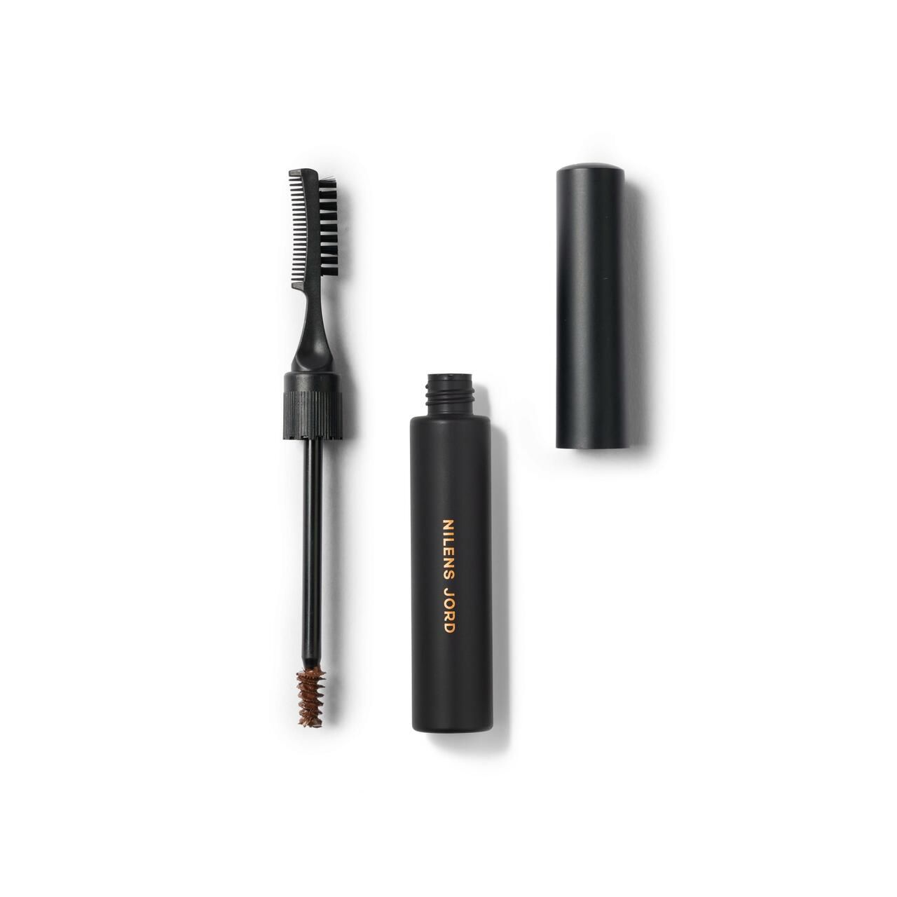 Schwarze Kosmetikflasche mit Pinsel und Bürste. Aufschrift: NILENS JORD. Deckel daneben.