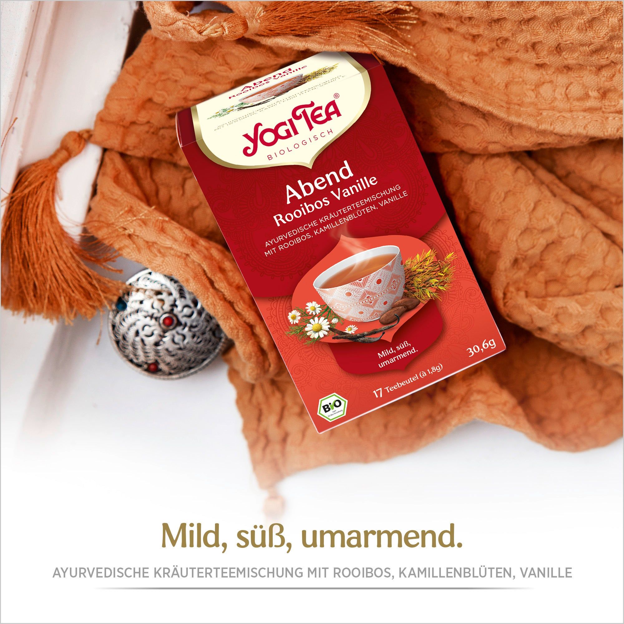 Yogi Tea Abend Rooibos Vanille Packung. Rote Verpackung mit Logo und Produktbezeichnung. Bio-Siegel. Auf orangefarbenem Tuch.