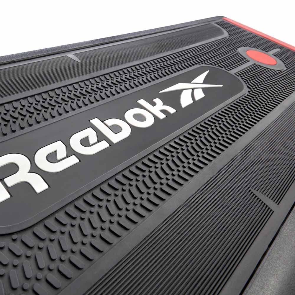 Schwarzer Reebok Step mit weißem Logo. Oberfläche mit strukturierten Bereichen und roter Akzentfarbe.
