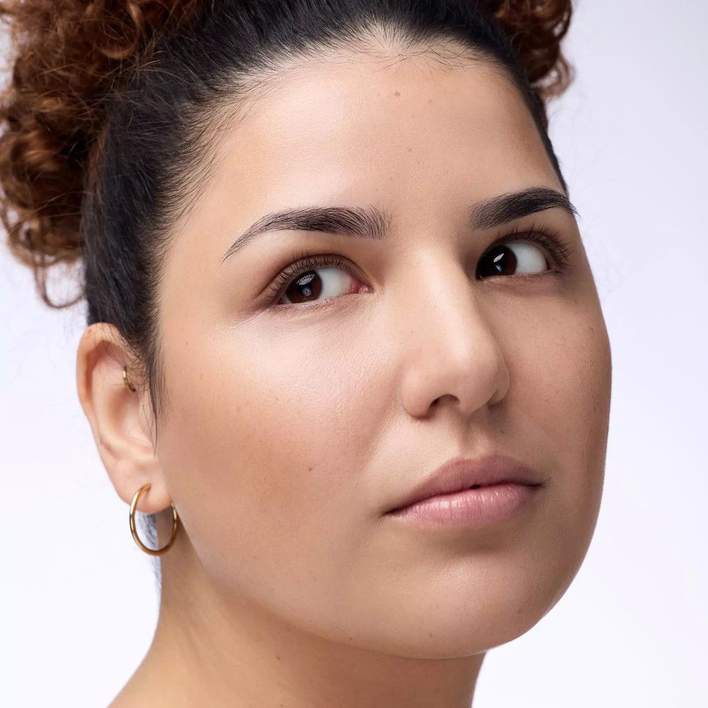 Porträt einer Frau. Sie blickt zur Seite. Hautton: hell. Hintergrund: hell.