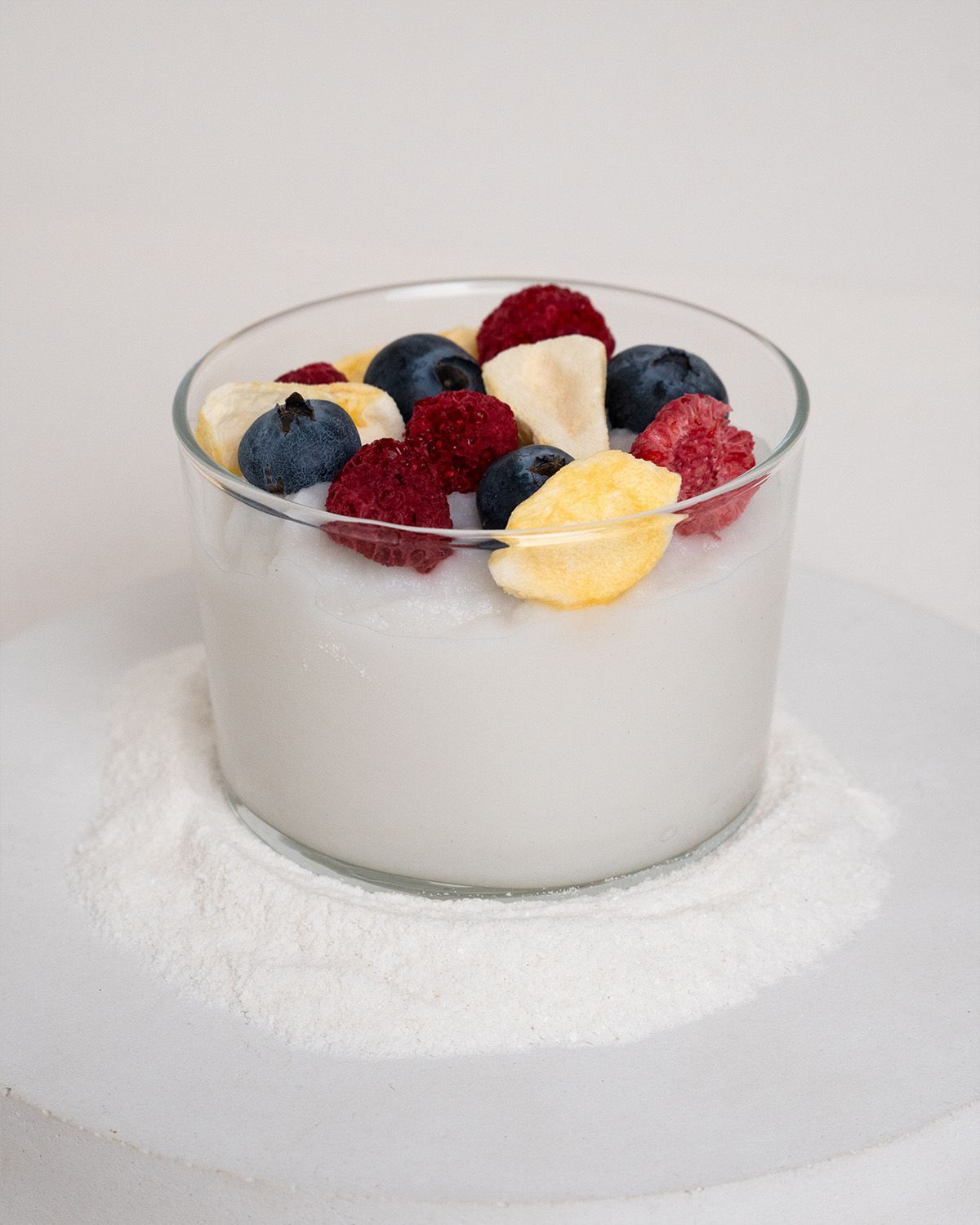 Glas mit weißem Reispudding, garniert mit Blaubeeren, Himbeeren und Bananenscheiben. Auf weißem Untergrund.