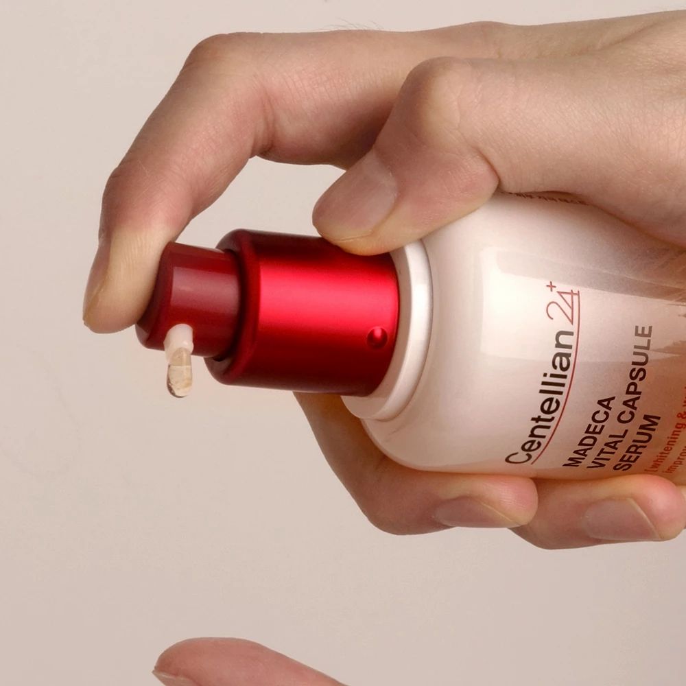 Hand hält Serumflasche. Roter Deckel, transparente Flüssigkeit mit gelben Kügelchen. Serum wird aus der Flasche gedrückt.