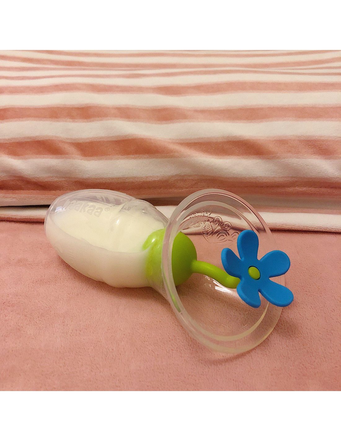 Milchpumpe mit blauem Blumenverschluss. Die Pumpe ist teilweise gefüllt. Liegt auf einer rosa Oberfläche.
