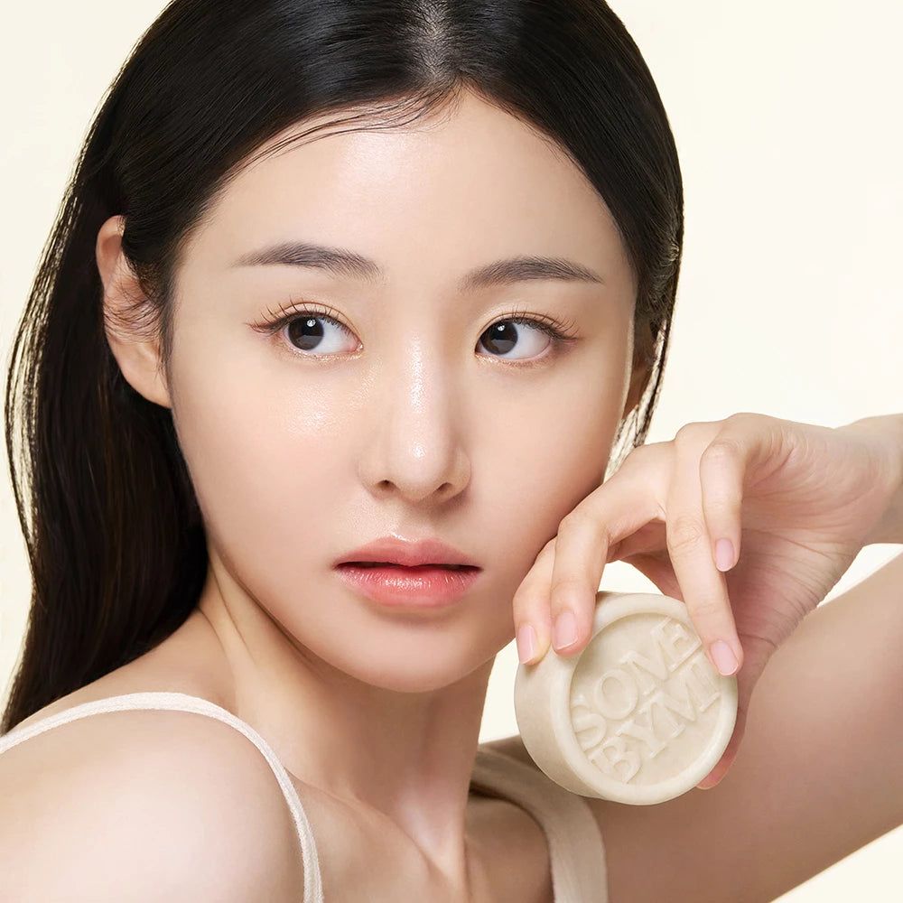 Eine Frau hält eine runde Seife mit dem Schriftzug SOME BYMI. Sie berührt ihr Gesicht mit der Seife.